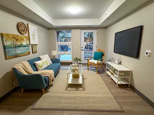 A living room with a blue couch, a chair, a coffee table, and a flat screen TV mounted on the wall.