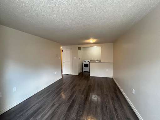 A spacious room with wood flooring and white walls.