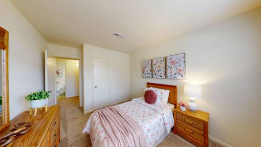 A bedroom with a pink bedspread and a wooden dresser.