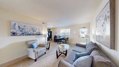 A living room with a grey couch and a painting on the wall.