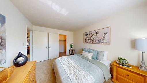 A bedroom with a bed, nightstand, and a painting on the wall.