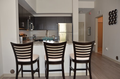 a kitchen and dining area with three chairs in front of a bar with a counter