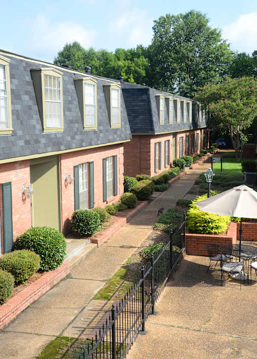 A black iron fence separates a small patio from a brick building.