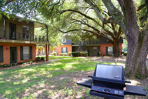 A grill is in the foreground of a grassy area with houses in the background.