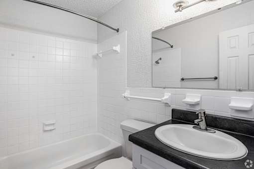 A white tiled bathroom with a black countertop and a white sink.