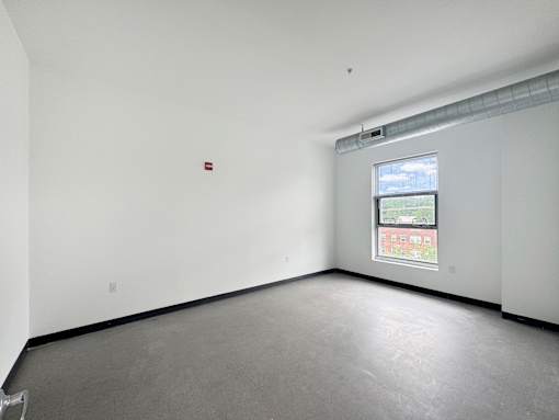A large empty room with a window and a fire extinguisher on the wall.