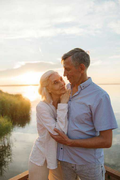 A couple is standing close together on a dock by the water during sunset.