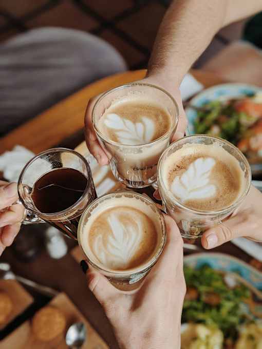 Four hands holding glasses of coffee with latte art.