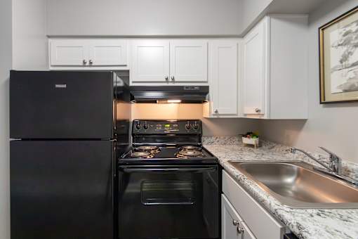 A black refrigerator is in a kitchen with a stove and oven in a 1 bedroom, 1 bath 560 square foot apartment at Aspen Village Apartments in the Westwood neighborhood of Cincinnati, OH.