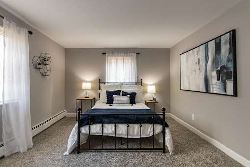 A bedroom with a bed, two lamps, and a painting on the wall in a 1 bedroom, 1 bath 560 square foot apartment at Aspen Village Apartments in the Westwood neighborhood of Cincinnati, OH.