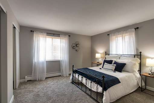 A bedroom with a bed, nightstands, and a window with curtains in a 1 bedroom, 1 bath 560 square foot apartment at Aspen Village Apartments in the Westwood neighborhood of Cincinnati, OH.