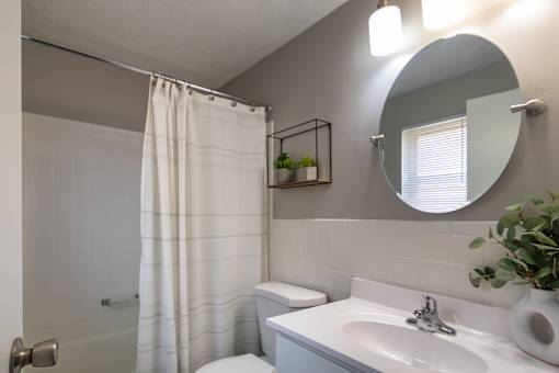 A bathroom with a white shower curtain and a white toilet in a 1 bedroom, 1 bath 560 square foot apartment at Aspen Village Apartments in the Westwood neighborhood of Cincinnati, OH.