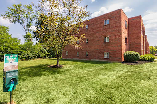 Open green lawn with pet waste station beside a brick apartment building at Aspen Village