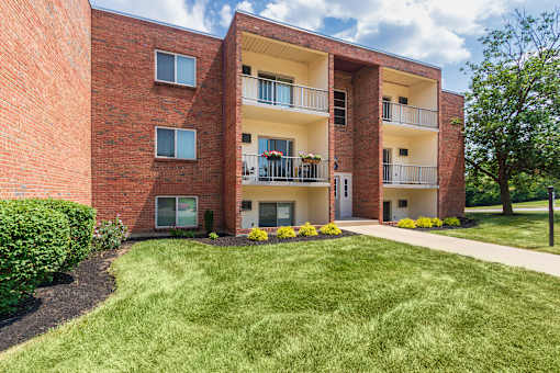 Apartment building exterior with balconies, landscaped beds, and green lawn at Aspen Village