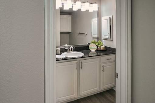 Bathroom vanity with white cabinetry, dark countertop, and framed mirror in a one-bedroom apartment home