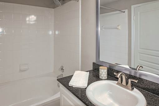 Bathroom with tub-shower combination, white vanity, and dark countertop at The Brownstones in Dallas