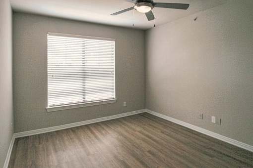 Bedroom with window, ceiling fan, and wood-look flooring in a one-bedroom apartment at The Brownstones