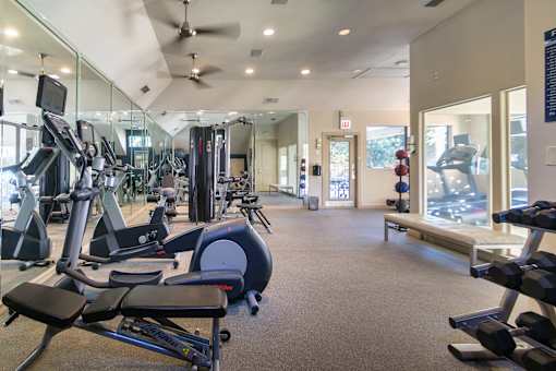 The 24-hour fitness center with treadmills, elliptical machines, and free weights at The Brownstones Townhome Apartments in the Far North Dallas neighborhood of Dallas, TX..