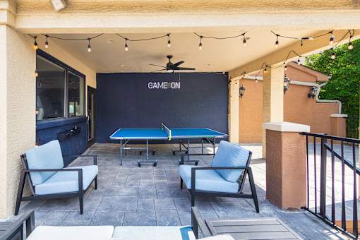 A pool table with a sign that says "Game On" is surrounded by chairs.