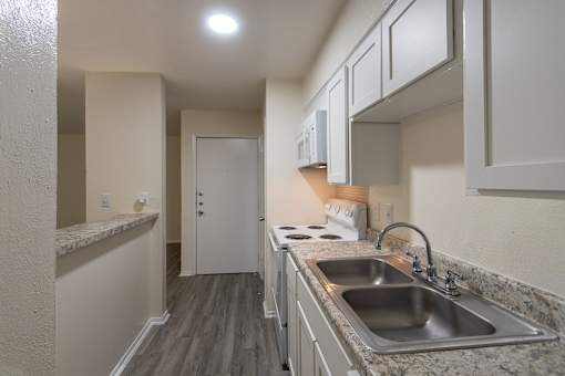 Kitchen with white cabinets and appliances in a 1 bedroom, 1 bath 752 sq ft apartment home with hardwoodlike flooring throughout at The Biltmore Apartments located in the Vickery Midtown neighborhood of Dallas, TX.