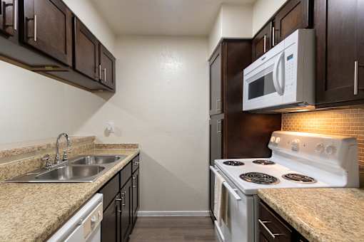 A kitchen with dark wood cabinets and white appliances in a 1 bedroom, 1 bath B, 629 sq ft apartment home at The Biltmore Apartments located in the Vickery Midtown neighborhood of Dallas, TX.