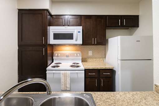 A kitchen with dark wood cabinets and white appliances in a 1 bedroom, 1 bath B, 629 sq ft apartment home at The Biltmore Apartments located in the Vickery Midtown neighborhood of Dallas, TX.