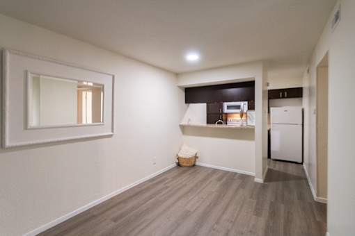 View of the dining area with large mirror looking into a kitchen with dark wood cabinets and white appliances in a 1 bedroom, 1 bath B, 629 sq ft apartment home at The Biltmore Apartments located in the Vickery Midtown neighborhood of Dallas, TX.