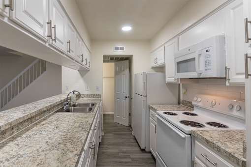 Kitchen with white cabinets and white appliances and large pass-through window in a 2 bedroom, 1.5 bath 1084 sq ft, 2-floor townhome at The Biltmore Apartments located in the Vickery Midtown neighborhood of Dallas, TX.