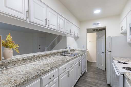 Kitchen with white cabinets and white appliances and large pass-through window in a 2 bedroom, 1.5 bath 1084 sq ft, 2-floor townhome at The Biltmore Apartments located in the Vickery Midtown neighborhood of Dallas, TX.