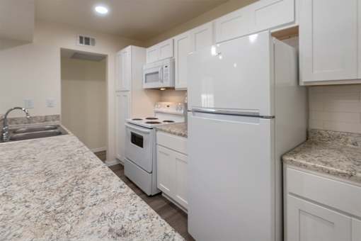 A kitchen with white appliances and cabinets with hardwoodlike flooring throughout in a 2 bedroom, 2 bath 991 sq ft apartment home at The Biltmore Apartments located in the Vickery Midtown neighborhood of Dallas, TX.