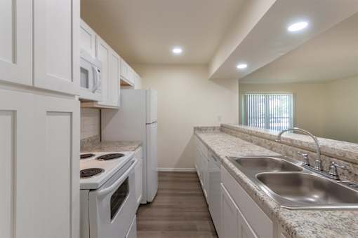 A kitchen with white appliances and cabinets with hardwoodlike flooring throughout in a 2 bedroom, 2 bath 991 sq ft apartment home at The Biltmore Apartments located in the Vickery Midtown neighborhood of Dallas, TX.