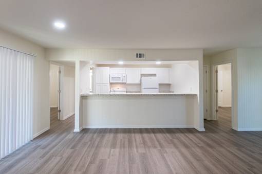 A kitchen with white appliances and cabinets with hardwoodlike flooring throughout viewed from the living room in a 2 bedroom, 2 bath 991 sq ft apartment home at The Biltmore Apartments located in the Vickery Midtown neighborhood of Dallas, TX.