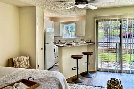 Open living and kitchen area in an Efficiency apartment at Cambridge Court Apartments in Dallas, Texas, showing the breakfast bar, patio door, and natural light.