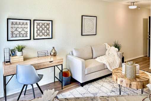 Living area in an Efficiency apartment at Cambridge Court Apartments in Dallas, Texas, showing a sofa, desk area, carpeted flooring, and neutral walls\.