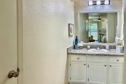 Bathroom vanity in an Efficiency apartment at Cambridge Court Apartments in Dallas, Texas, featuring white cabinetry, mirror, sink, and counter space.
