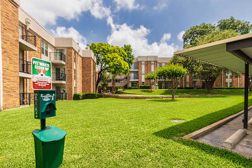A green trash can is in front of a sign that says Pet Waste Cleanup.