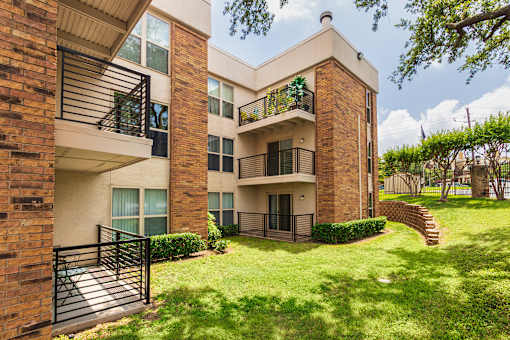 A brick building with a balcony and a green lawn in front.