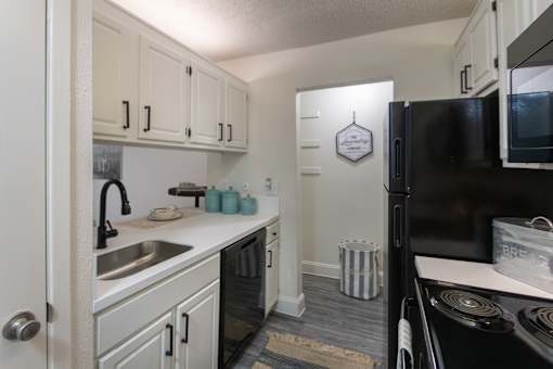 Kitchen in a 1-bedroom apartment at Cambridge Court Apartments in Dallas, Texas, featuring white cabinetry, black appliances, sink, and counter space.