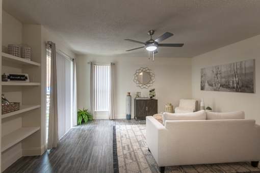 Living room in a 1-bedroom apartment at Cambridge Court Apartments in Dallas, Texas, showing wood-style flooring, a patio door, built-in shelving, and staged seating.