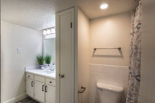 Bathroom in a 1-bedroom apartment at Cambridge Court Apartments in Dallas, Texas, showing vanity storage, mirror, toilet, towel bar, and tub/shower area.