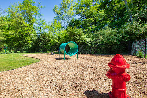 A fake, red fire hydrant stands in a dog park with a green agility tunnel, see saw and jump rings at Deer Hill Apartments in the Mount Washington neighborhood of Cincinnati, OH.