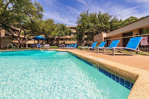Sparkling pool with clear blue water and lounge chairs at Harvard Square Apartments in Dallas