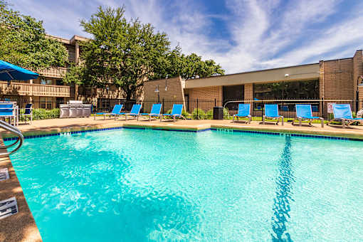 Outdoor pool with sunlit water and poolside seating and community grill at Harvard Square Apartments