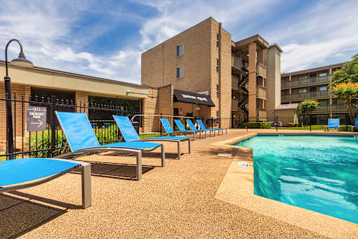 Pool deck with blue lounge chairs and apartment buildings at Harvard Square Apartments in Dallas