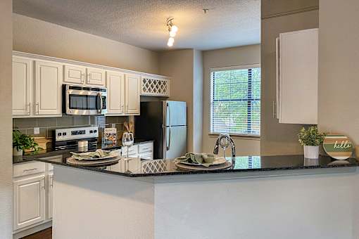 A kitchen with a black granite counter top and white cabinets in the 1486 square foot 3 bedroom, 3 bath apartment with attached 2-car garage at The Brownstones in Far North, Dallas, Texas