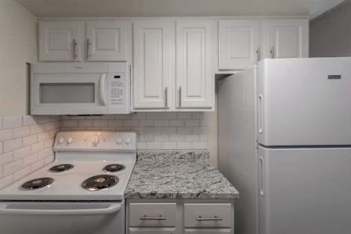 A kitchen with a white cabinets 1 bedroom, 1 bath apartment home and white appliances at Princeton Court Apartments in the Vickery Midtown neighborhood of Dallas, TX.