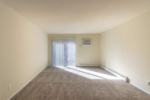 A room with a carpeted floor and a window with blinds.