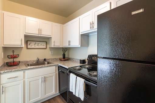 A black refrigerator in a kitchen with white cabinets.