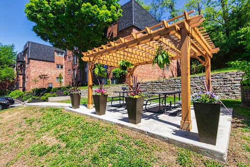A wooden pergola with hanging plants is in front of a apartment buildings at Romaine Court Apartments in the Oakley neighborhood of Cincinnati, Ohio.