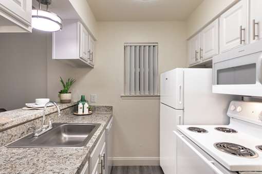 alley kitchen with white cabinets, granite-style countertops, electric range, and refrigerator in a 558-square-foot one-bedroom apartment